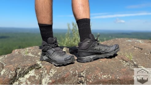 Wearing Salomon X Ultra 5 at top of summit on rocks blue sky behind