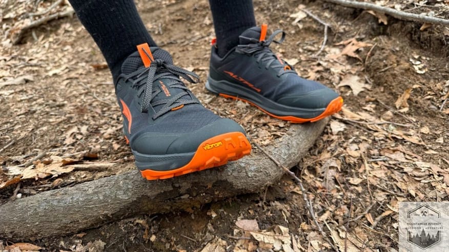 Front view of the Altra Lone Peak 9+ trail shoe showing the wide FootShape toe box and reinforced toe bumper while balanced on a tree root.