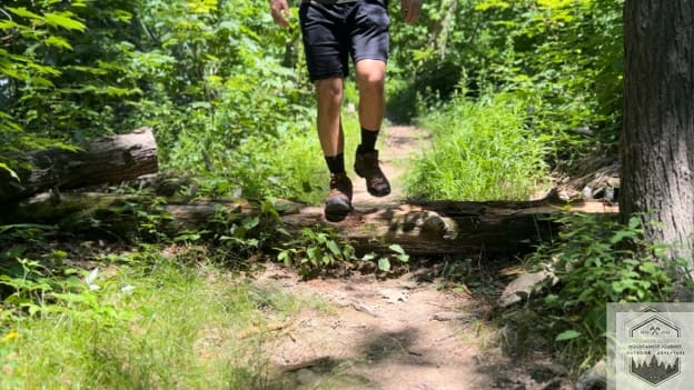 blog-img-1721426514523 Testing the Merrell Moab 3's torsional stability while stepping over a log, highlighting the molded nylon arch shank that provides midfoot support on uneven forest obstacles.
