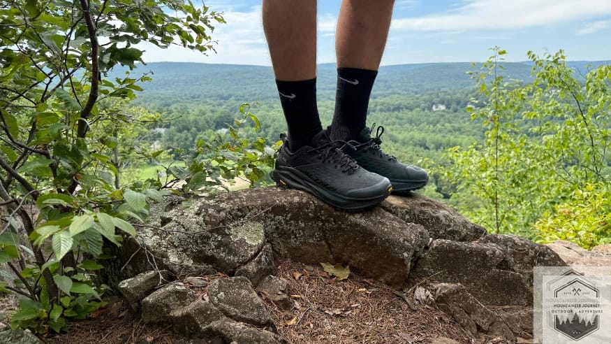 Standing at top the a rock wearing the altra olympus 6 with summit in background