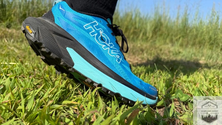 Side profile of Hoka Mafate 5 running shoe on grass highlighting the massive stack height.
