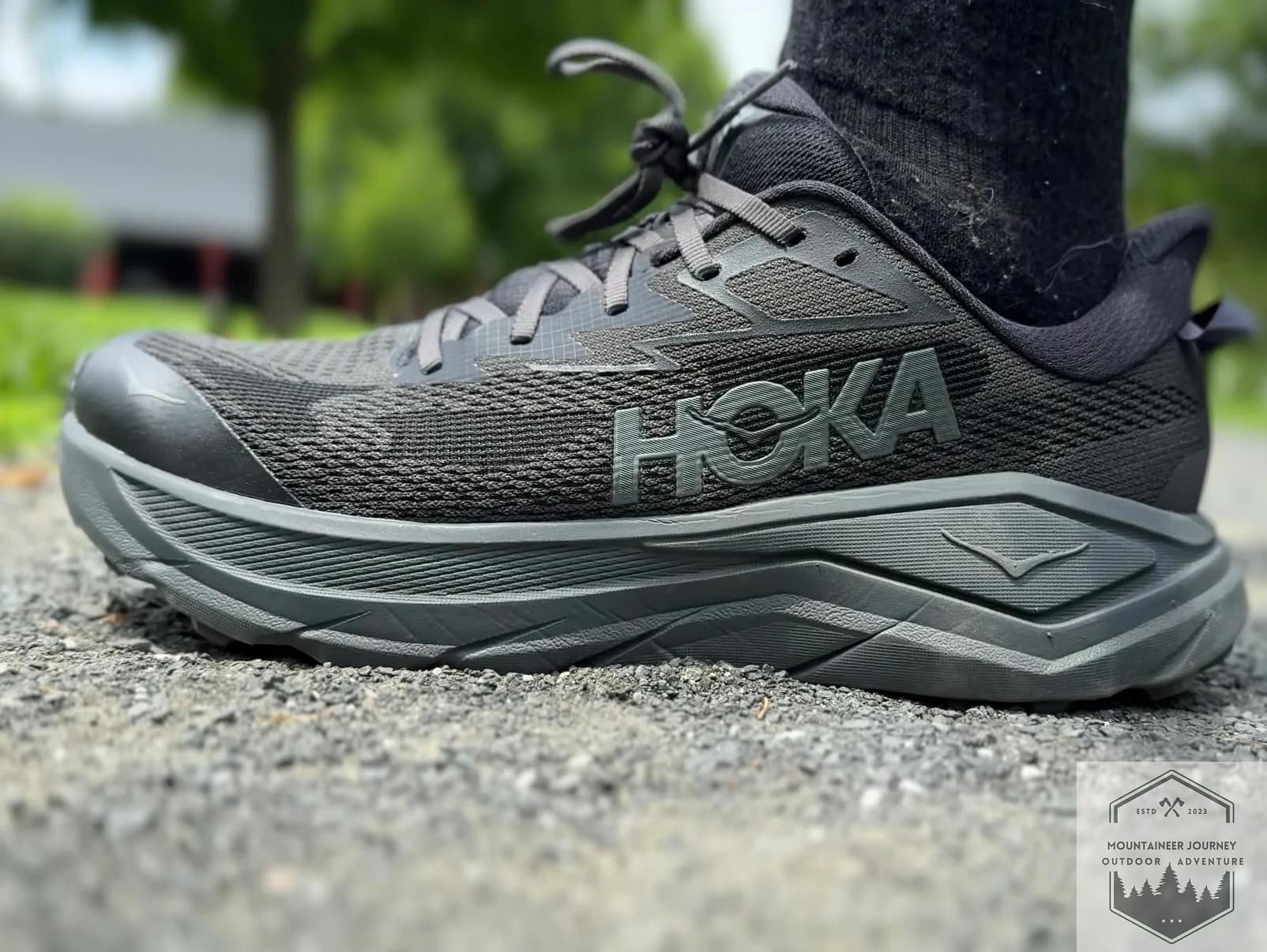 Full side view of the Hoka Challenger 8 trail shoe on a gravel surface, showcasing the maximalist CMEVA midsole and the versatile road-to-trail design.