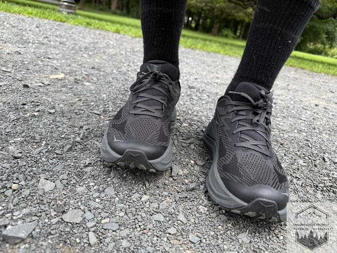 Front view of the Hoka Challenger 8 on a dirt trail, highlighting the breathable rPET engineered mesh upper and the protective 3D-printed toe cap overlays.