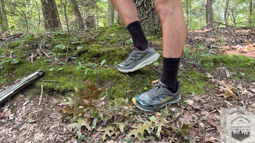 Top-down view of the Hoka Stinson 7 standing in autumn leaves, highlighting the high-volume midsole and protective engineered mesh upper.